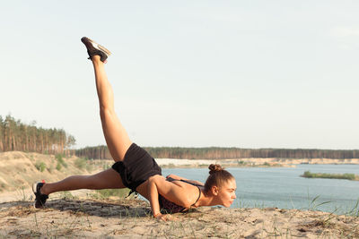 Woman in sports clothing exercising at beach during sunset