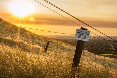 Barbed wire fence on field against sky during sunrise