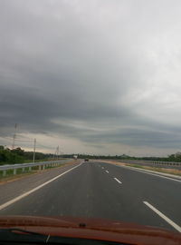 Road passing through highway against cloudy sky