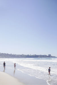 Mother with children enjoying vacation at beach against clear sky