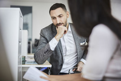 Mid adult businessman discussing with female coworker while sitting in office