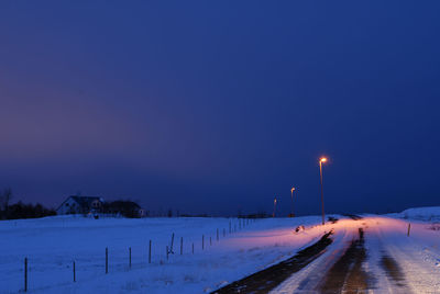 Road on snow covered field against clear blue sky at night