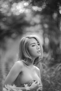 Topless seductive woman holding shirt while standing by plants