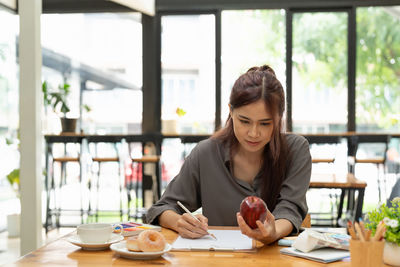 Woman holding apple while writing at desk in office