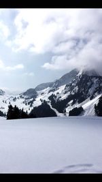 Scenic view of snow covered mountains against cloudy sky