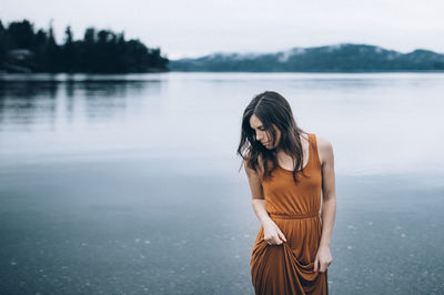 Woman looking down while standing in sea against sky