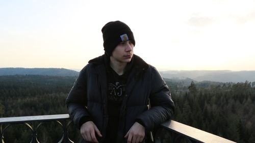 Young man sitting on railing against sky