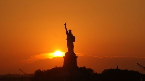 Silhouette statue of liberty against orange sky
