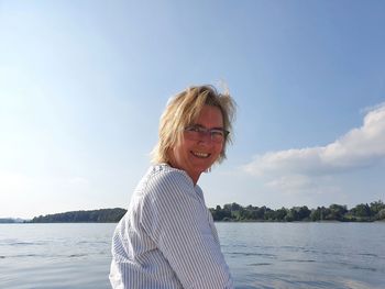 Portrait of smiling woman by water against sky