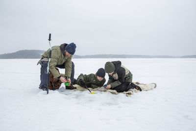 Boys doing fishing by mature man at frozen lake