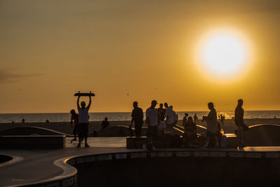 Silhouette people by sea against sky during sunset