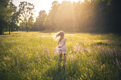 Back view of girl running on flower meadow at evening twilight