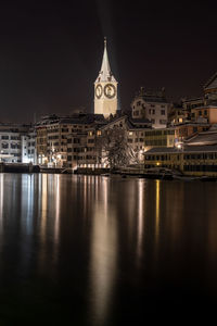 Illuminated buildings by river against sky in city at night