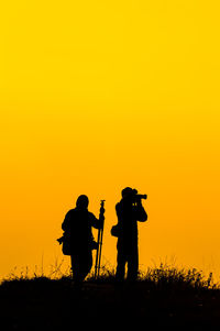 Silhouette people photographing on field against orange sky