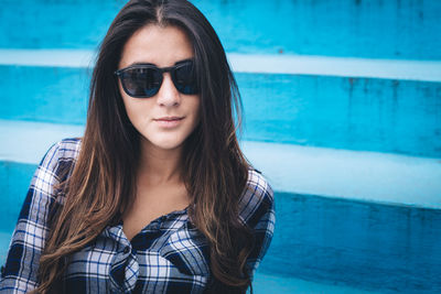 Portrait of beautiful young woman wearing sunglasses against wall