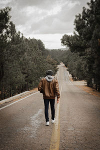 Rear view of man walking on road against sky