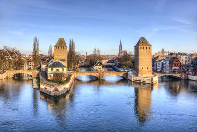 Bridge over river by buildings against sky in city