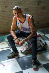 Full length portrait of young man sitting against wall