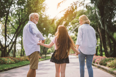 Rear view of girl with grandparents standing on road