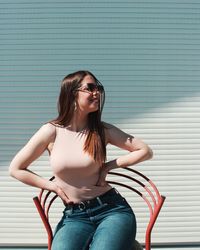 Beautiful young woman sitting on chair by shutter