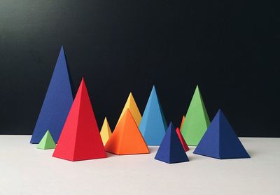 Multi colored paper pyramids on table against black wall