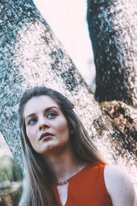 Low angle view of woman standing against tree trunk