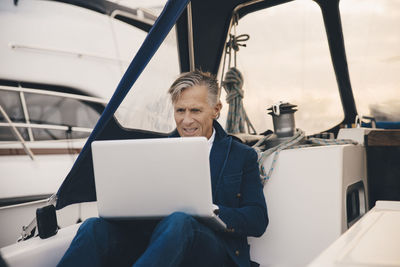 Senior man using laptop while sitting in yacht