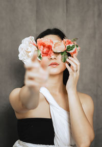 Young woman with flowers in front of face against wall