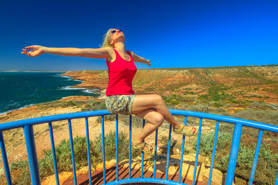 Woman with arms outstretched sitting on railing at kalbarri national park 