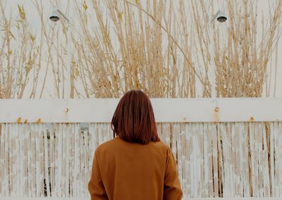 Rear view of woman standing against fence and plants