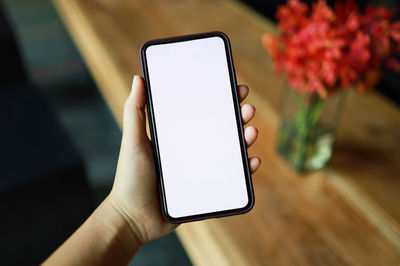 Close-up of hand holding mobile phone on table