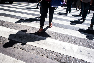 Low section of people crossing road during sunny day