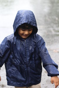 Boy in raincoat standing on street during rainfall