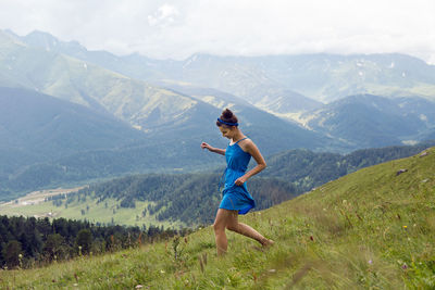 Woman in blue long dress standing on a high mountain in a meadow on a background of sheep