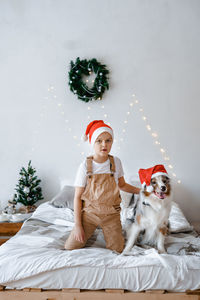A boy and a dog in red santa hat having fun on bed. best friends. christmas mood. festive atmosphere