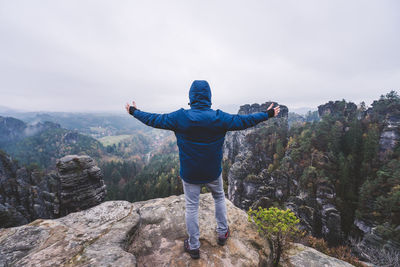 Rear view of man standing on rock against sky