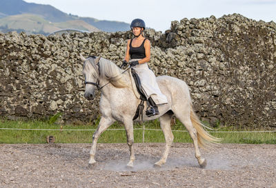 White lusitano mare, female dressage rider, outdoors on sand.