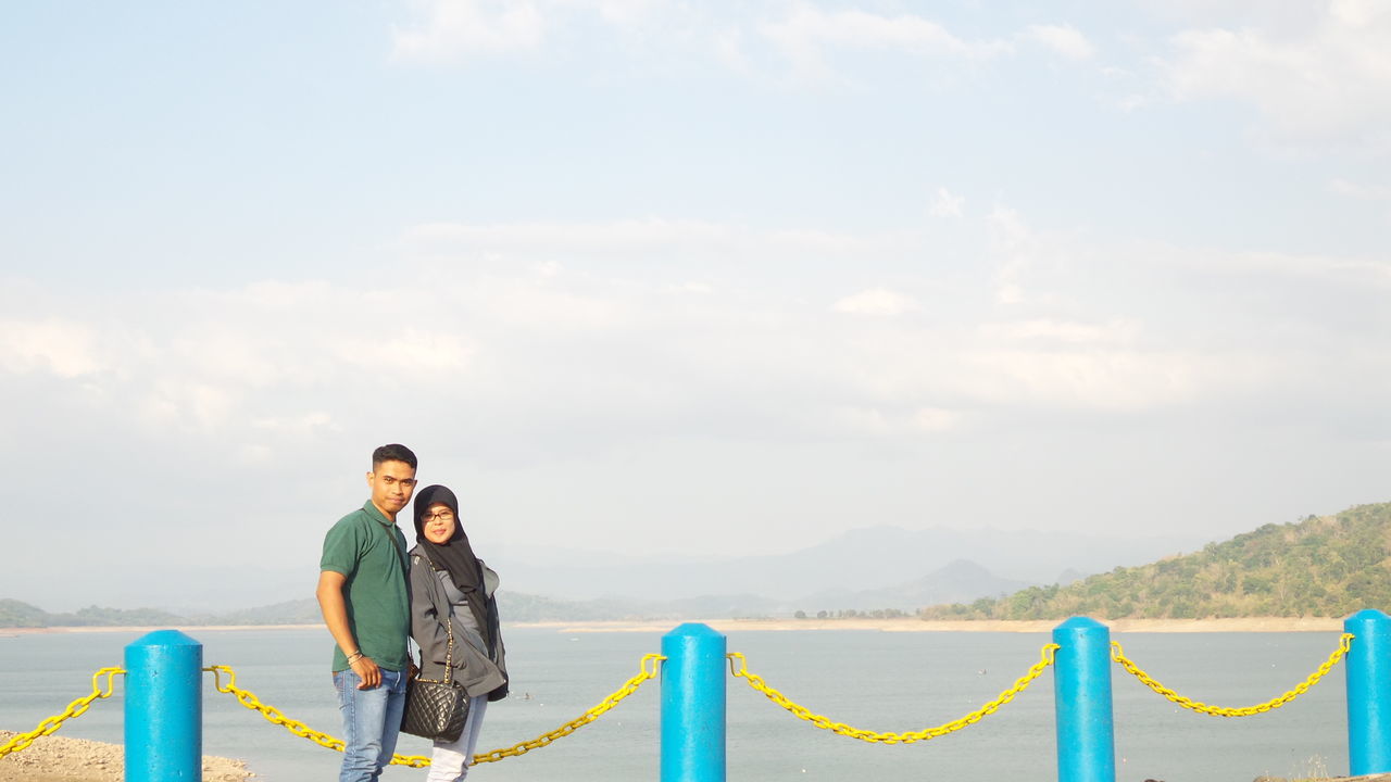 lifestyles, leisure activity, water, sky, sea, casual clothing, person, vacations, mountain, cloud - sky, railing, standing, beach, blue, rear view, sitting, scenics, nature