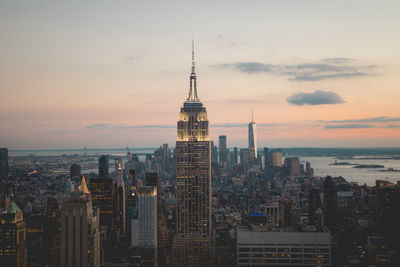 Empire state building amidst towers in city against sky during sunset