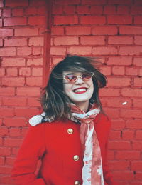 Portrait of smiling young woman against red brick wall