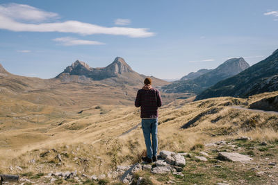 Rear view of man standing on rock against mountains and sky