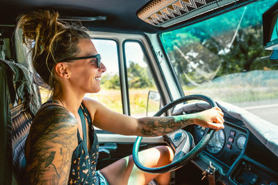 Side view of female traveler in sunglasses sitting at steering wheel during road trip in rv trailer in cantabria