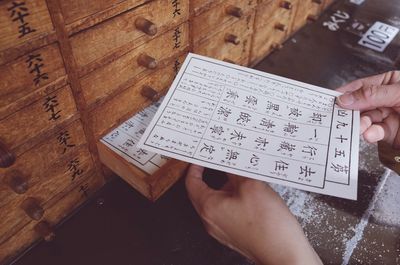 Cropped image of person holding fortune paper by wooden drawers