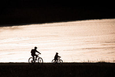 Man riding bicycle with son by lake during sunset