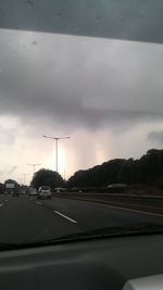 Cars on road against cloudy sky