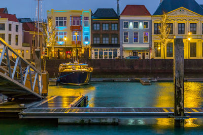Canal by illuminated buildings in city at night