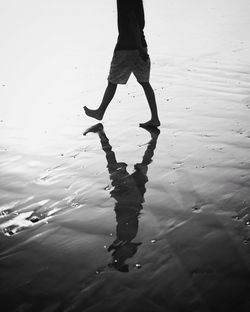 Low section of man walking on wet beach