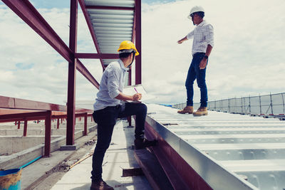 Man standing on railing by construction site against sky