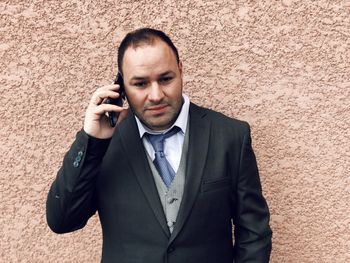 Businessman talking on mobile phone while standing against wall