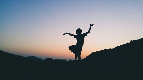 Low angle view silhouette of teenage boy standing against sky during sunset